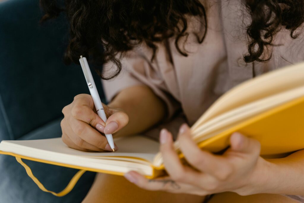 pexels-photo-7606033-7606033 Person writing in a yellow notebook indoors, focusing on ideas.